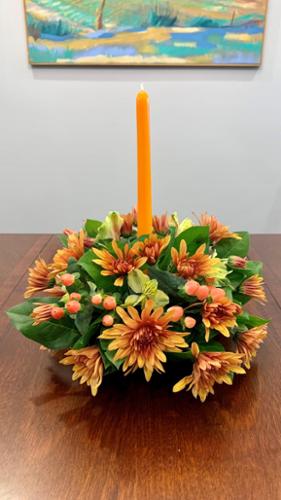 12" round centerpiece with a single taper candle. A combination of mums, alstroemerias, and hypericum varieties in fall colors make up this stunning arrangement. For a perfectly lit dinner table.